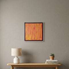 A framed abstract painting with vertical orange, yellow, and red brushstrokes hangs on a gray wall above a light wood console table in a styled room with a lamp, books, a small plant, and a woven basket.