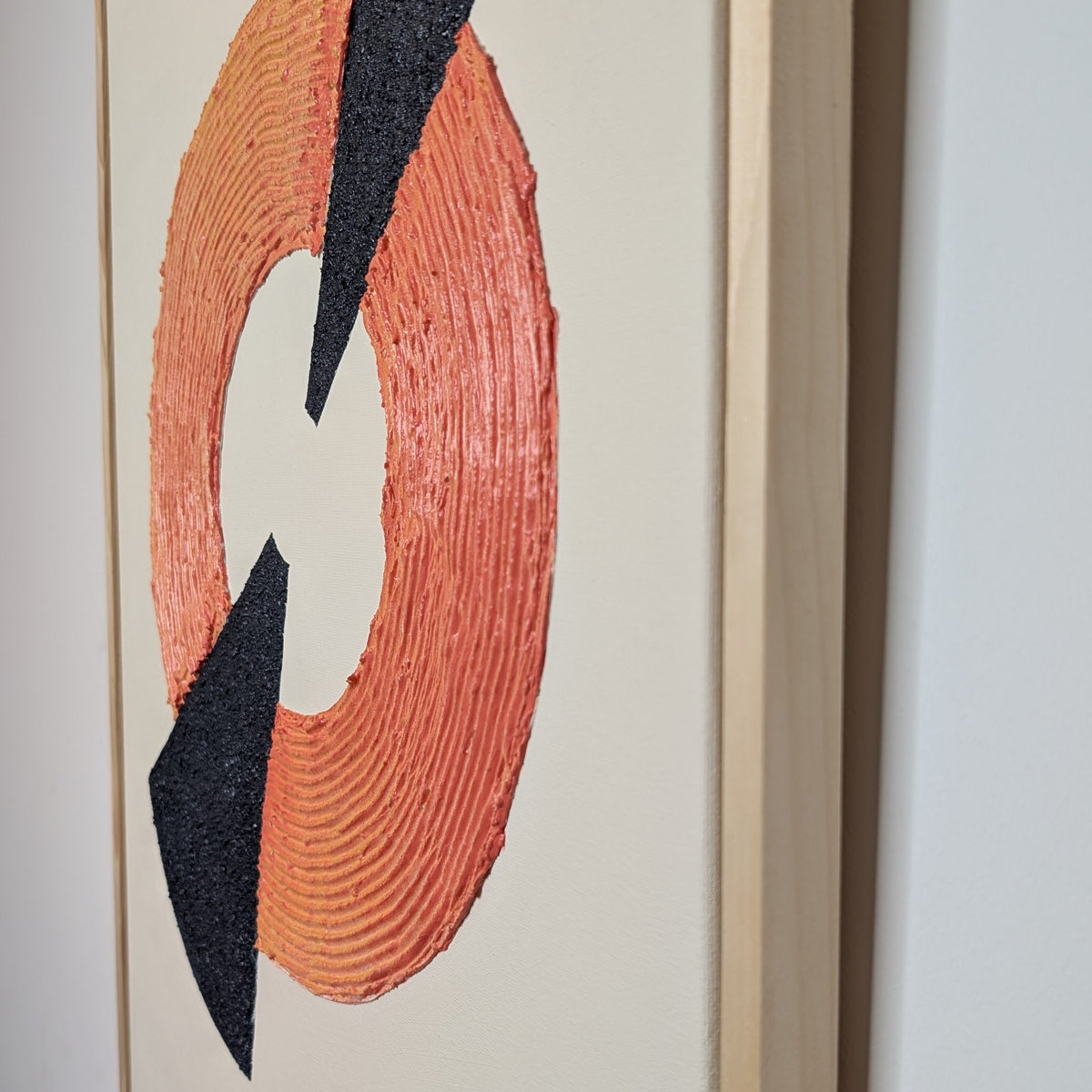 Framed abstract wall art featuring a textured orange ring with two navy blue triangular shapes on a cream background, shown hanging on a light gray wall.