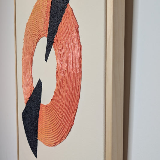 Framed abstract wall art featuring a textured orange ring with two navy blue triangular shapes on a cream background, shown hanging on a light gray wall.